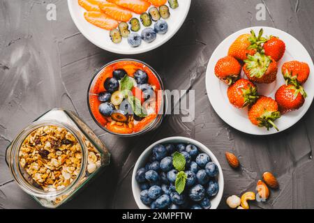 Parfait von Müsli, Joghurt und Beeren gesundes Frühstück, Müsli mit Erdbeeren und Heidelbeeren auf einem grauen strukturierten Hintergrund mit Zutaten gelegt Stockfoto