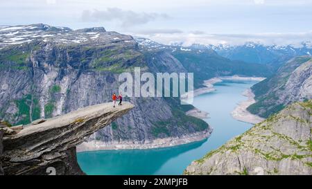 Zwei Personen stehen am Rande von Trolltunga, Norwegen, einer Klippe mit Blick auf einen ruhigen norwegischen See und die umliegenden Berge. Ein paar Männer und Frauen auf einem Berg in Norwegen Stockfoto