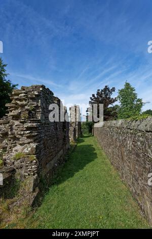 Der Rand der Balmerino Priory in der Nähe einer Village Stone Wall, mit den Ruinen in starkem Kontrast zur ordentlichen geraden Village Wall daneben. Stockfoto