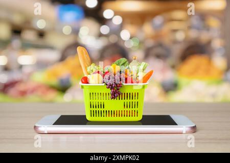 Frisches Essen und Gemüse im Warenkorb auf dem mobilen Smartphone auf Holztisch mit verschwommenem Hintergrund Supermarkt Gang Online-Konzept Stockfoto