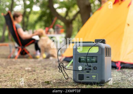 Tragbares Kraftwerk mit Lithium-Ferrophosphat-Batterie, das elektronische Geräte auflädt, die auf einem wilden Campingplatz vor dem gelben Zelt verwendet werden. Tragbar Stockfoto