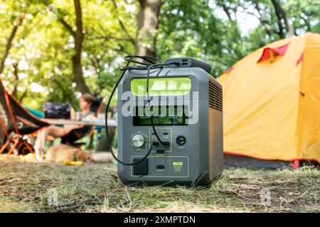 Tragbares Kraftwerk mit Lithium-Ferrophosphat-Batterie, das elektronische Geräte auflädt, die auf einem wilden Campingplatz vor dem gelben Zelt verwendet werden. Tragbar Stockfoto