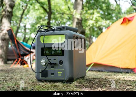 Tragbares Kraftwerk mit Lithium-Ferrophosphat-Batterie, das elektronische Geräte auflädt, die auf einem wilden Campingplatz vor dem gelben Zelt verwendet werden. Tragbar Stockfoto
