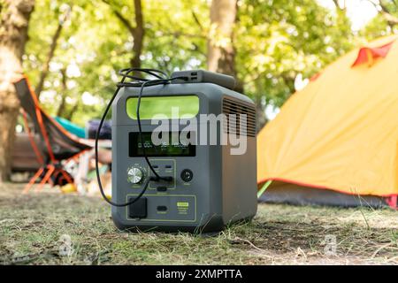 Tragbares Kraftwerk mit Lithium-Ferrophosphat-Batterie, das elektronische Geräte auflädt, die auf einem wilden Campingplatz vor dem gelben Zelt verwendet werden. Tragbar Stockfoto