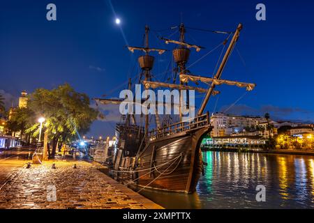 NAO Victoria Carrack Segelschiff Nachbildung bei Nacht, an der Uferpromenade in Sevilla, Spanien. Historisches spanisches Schiff, das den ersten Circumnavi machte Stockfoto