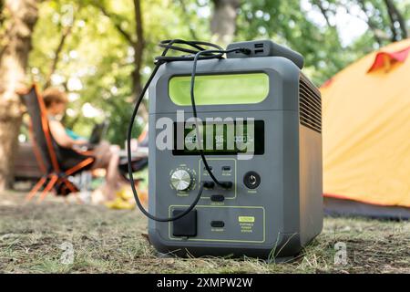 Tragbares Kraftwerk mit Lithium-Ferrophosphat-Batterie, das elektronische Geräte auflädt, die auf einem wilden Campingplatz vor dem gelben Zelt verwendet werden. Tragbar Stockfoto