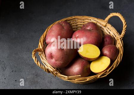 Schöne rosa neue Kartoffeln in einem Korb auf dunklem Hintergrund Stockfoto