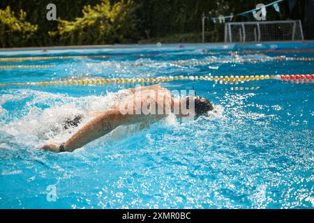 Ein Foto von der Seite des Schwimmers mit einer Schutzbrille führt einen kräftigen Schmetterlingsschlag im Pool aus und erzeugt Spritzer, während er entschlossen vorwärts geht. Stockfoto