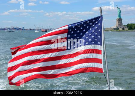 Die Stars & Stripes auf dem Heck eines der Kreuzfahrtschiffe, die Touristen zu Liberty & Ellis Islands im Hafen von New York, USA, bringen. Stockfoto