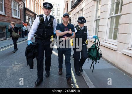 London, Großbritannien. Juli 2024. Ein Demonstrant wird verhaftet, als Klimaktivisten der Extinction Rebellion die Büros des rechten Think Tank Policy Exchange in der Old Queen Street besetzen, die Straße mit einem Stativ blockieren und außerhalb des Gebäudes „Ölspritzen“ verursachen. Der Protest war Teil der Kampagne „Cut the Bands“ to fossile Brennstoffe, die angeblich unangemessenen Einfluss der Öl- und Gasunternehmen auf die Regierung über Think Tanks vorwarf, was zu unzureichenden Maßnahmen zur Bewältigung des Klimanotfalls führte. Quelle: Ron Fassbender/Alamy Live News Stockfoto