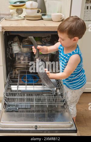 Das Baby lädt den Geschirrspüler in die Küche. Das Kind hilft Eltern bei der Hausarbeit. Kind im Alter von drei Jahren (dreijähriger Junge) Stockfoto