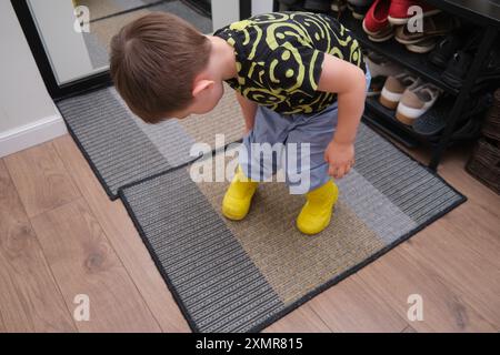 Ein Kind zieht Schuhe an, die im Flur stehen. Das Baby zieht gelbe Stiefel an, um spazieren zu gehen. Kind im Alter von 3 Jahren (dreijähriger Junge) Stockfoto