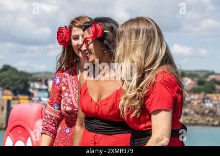 Drei junge Frauen ruhen sich aus, nachdem sie zum Kate Bush Day auf Folkestones Harbour Arm getanzt haben Stockfoto