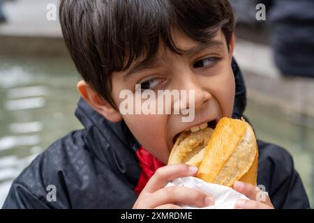 Junge beißt traditionelles Tintenfisch-Sandwich draußen auf dem Major Square in der Innenstadt von Madrid Stockfoto