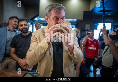 München, Deutschland. Juli 2024. Markus Söder (CSU), Ministerpräsident Bayerns, beißt in einem Dönerrestaurant einen frischen Döner. Söder hatte zuvor Kebabs an Instagram-Fans verlost. Quelle: Peter Kneffel/dpa/Alamy Live News Stockfoto