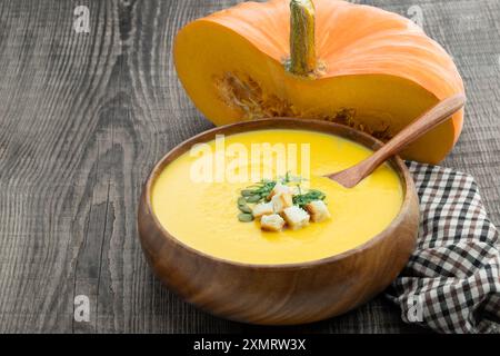 Kürbiscremesuppe mit Croutons in einer Holzschale auf rustikalem Tisch Stockfoto