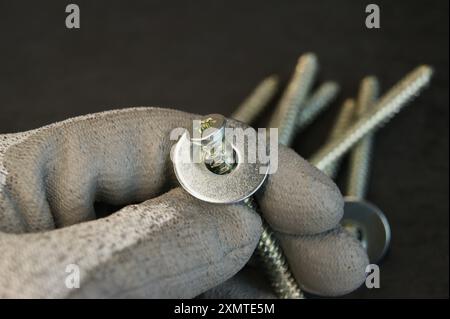 Arbeitsprozess des Monteurs. Neue Befestigungsschraube mit Stahlscheiben in der Hand des Montagewerkzeugs. Stockfoto