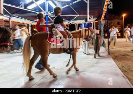 Kinder genießen einen Ponyritt auf einem Nachtkarussell in Sanlucar de Barrameda, Andalusien. Spaß und Spannung auf einer lokalen Messe. Stockfoto