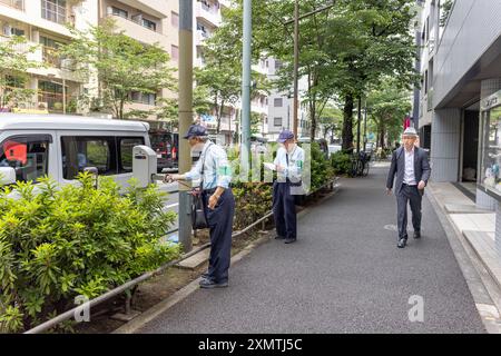 Nakano (Japan) – 24. Mai 2024: Zwei alte japanische Offiziere sammeln Geld am Parkautomaten in Nakano City (Tokio). Stockfoto