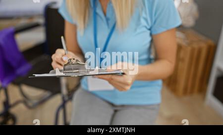 Eine blonde Frau in einer Klinik, die auf ein Klemmbrett schreibt, ein Beispiel für einen Arzt in einem Innenbereich. Stockfoto