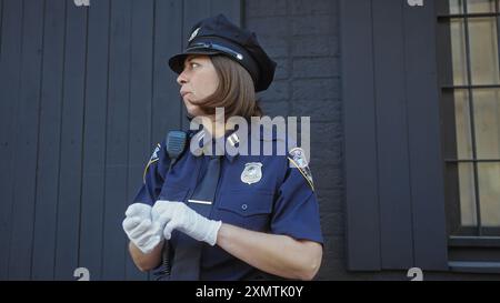 Profilansicht einer fokussierten Polizistin, die draußen in einer Stadt steht, Uniform und Handschuhe trägt Stockfoto