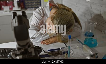 Erschöpfte junge Wissenschaftlerin schläft in einem unordentlichen Labor, inmitten von Forschungsgeräten. Stockfoto