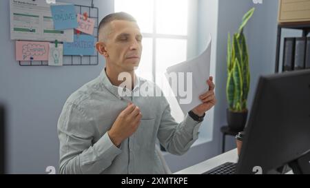 Junger Mann in einem Büro, der Dokumente mit geschlossenen Augen hält, konzentriert und entspannt wirkt, mit motivierenden Postern und Pflanzen im Hintergrund. Stockfoto