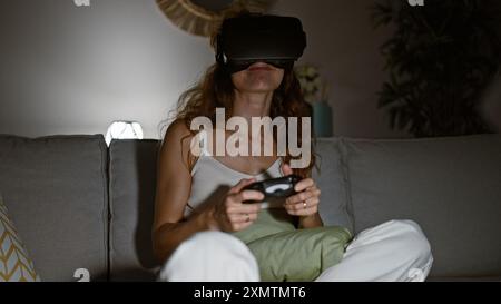 Eine junge Frau genießt Virtual-Reality-Spiele in einem gemütlichen Wohnzimmer, Controller in der Hand. Stockfoto