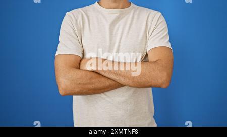 Lässiger, selbstbewusster hispanischer Mann mit überkreuzten Armen steht vor einem durchsichtigen blauen Hintergrund. Stockfoto