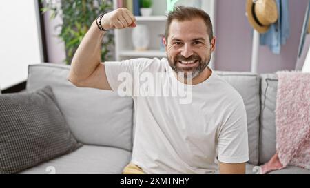 Lächelnder Mann mittleren Alters mit grauem, flexiblem Arm in einem modernen Wohnzimmer. Stockfoto