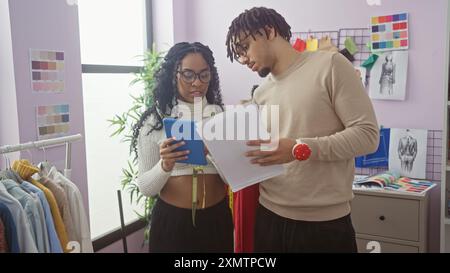 Eine Frau mit einem Tablet und ein Mann mit Modedesigns arbeiten in einem lebendigen Atelier zusammen. Stockfoto