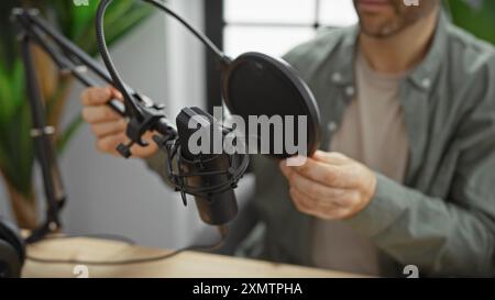 Ein junger hispanischer Mann stellt ein Mikrofon in einem Radiostudio ein und verkörpert damit moderne Rundfunksendungen. Stockfoto