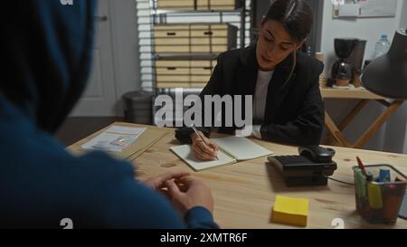 Die Ermittlerin verhört einen Mann in einem Büro, mit Pässen und einem Notizblock auf dem Schreibtisch. Stockfoto