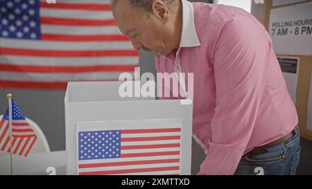 Mann mittleren Alters, der in einer us-Wahlstation mit amerikanischen Fahnen abstimmt, was Demokratie und Staatsbürgerschaft bedeutet. Stockfoto