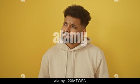 Nachdenklicher afroamerikanischer Mann in lässigem Hoodie vor leuchtendem gelbem Hintergrund, der nachdenklich aussieht. Stockfoto