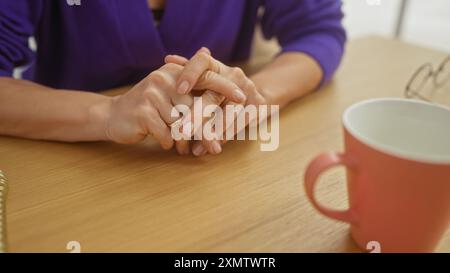 Eine Nahaufnahme der Hände einer kaukasischen Frau auf einem Holztisch mit einem roten Becher in einem gemütlichen Zimmer. Stockfoto