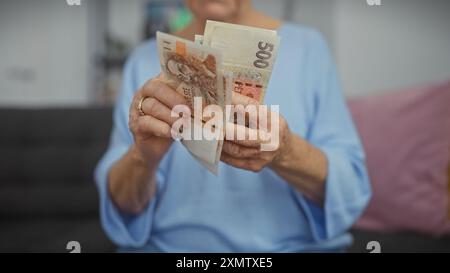 Reife Frau hält tschechische Kronen-Banknoten drinnen und zeigt Geld mit verschwommenem Hintergrund Stockfoto