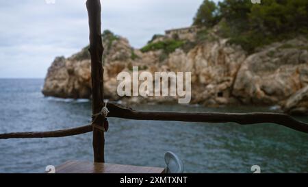 Rustikaler Holzbalkon mit Blick auf die ruhige cala deia auf mallorca mit schroffen Klippen, ruhigem blauem Meer und üppigem Grün Stockfoto