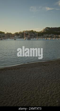 Abendlicher Blick auf den Hafen, der sich der Dämmerung nähert, mit Booten, die auf ruhigen Gewässern und an den Hügeln gelegenen Gebäuden in Port de soller, mallorca, angedockt werden Stockfoto