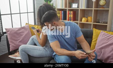Eine Frau schreibt am Telefon, während ein Mann neugierig in einem gemütlichen Wohnzimmer umschaut. Stockfoto