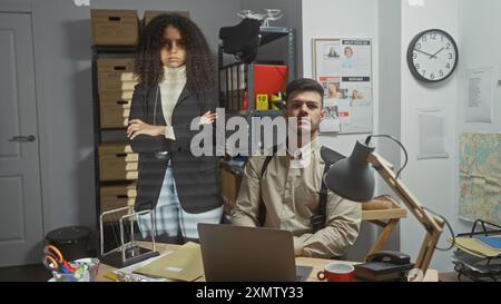 Zwei Ermittler, ein Mann und eine Frau, posierten in einem überfüllten Detektivbüro voller Beweise und Karten. Stockfoto