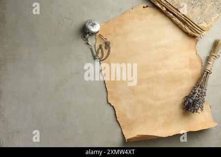 Blatt altes Pergamentpapier, Lavendelblumen, Vintage-Buch und Taschenuhr mit Kettenkette auf grauem Tisch, flach gelegen Stockfoto