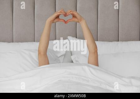 Guten Morgen. Frau macht Herzgeste mit Händen im Bett, Nahaufnahme Stockfoto