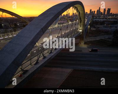 Blick auf das Bogensegment auf der 6th Street Viaduct Bridge über den Los Angeles River mit der Skyline der Innenstadt in der Ferne bei Sonnenuntergang Stockfoto