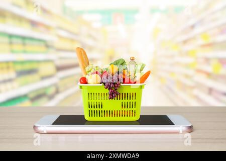 Frisches Essen und Gemüse im Warenkorb auf dem mobilen Smartphone auf Holztisch mit verschwommenem Hintergrund Supermarkt Gang Online-Konzept Stockfoto