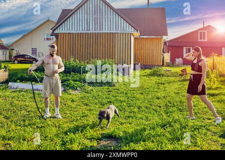 Der amerikanische Bully Dog spielt mit Wassersprays aus dem Gartenschlauch während eines Spaziergangs mit seinen jungen Besitzern im Hinterhof des Landhauses. Stockfoto