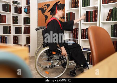 Männlicher Absolvent im Rollstuhl, der Buch aus dem Regal in der Bibliothek nimmt Stockfoto