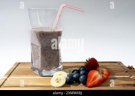 Frische Erdbeeren, Heidelbeeren und Bananen werden auf einem hölzernen Schneidebrett zubereitet und zu einem köstlichen Smoothie gemischt. Stockfoto