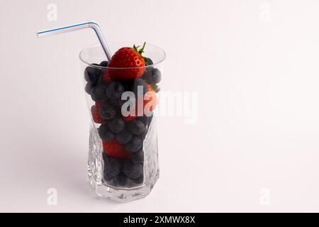 Ein klares Glas gefüllt mit lebendigen, frischen Beeren und einem schmalen Strohhalm. Es symbloisiert die Zutaten in einem gesunden Smoothie. Stockfoto