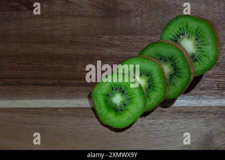 Vier Kiwi-Scheiben, die ordentlich auf einem Holztisch angeordnet sind, zeigen ihr leuchtendes grünes Fleisch und ihre schwarzen Samen. Die natürlichen Texturen der Kiwi stehen im Kontrast zu wi Stockfoto